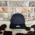 Black cap with a logo on a cowhide rug against a brick wall