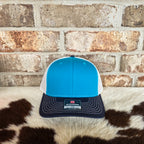 Blue Teal, Birch, and Navy cap on a cowhide rug with a brick wall background