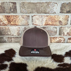 Brown cap with a logo on a cowhide rug against a brick wall