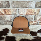 Brown and black trucker hat with Richardson logo on a cowhide rug against a brick wall.