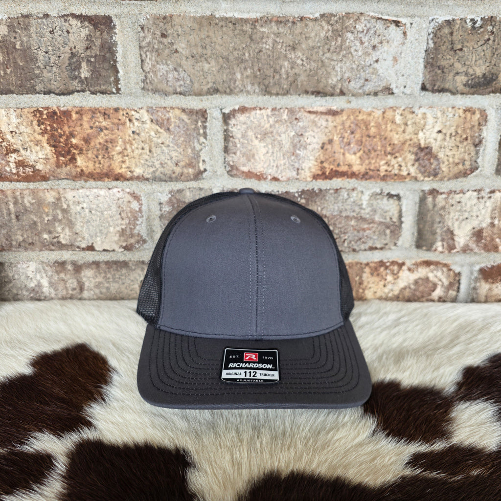 Gray trucker cap with a logo on a cowhide rug against a brick wall