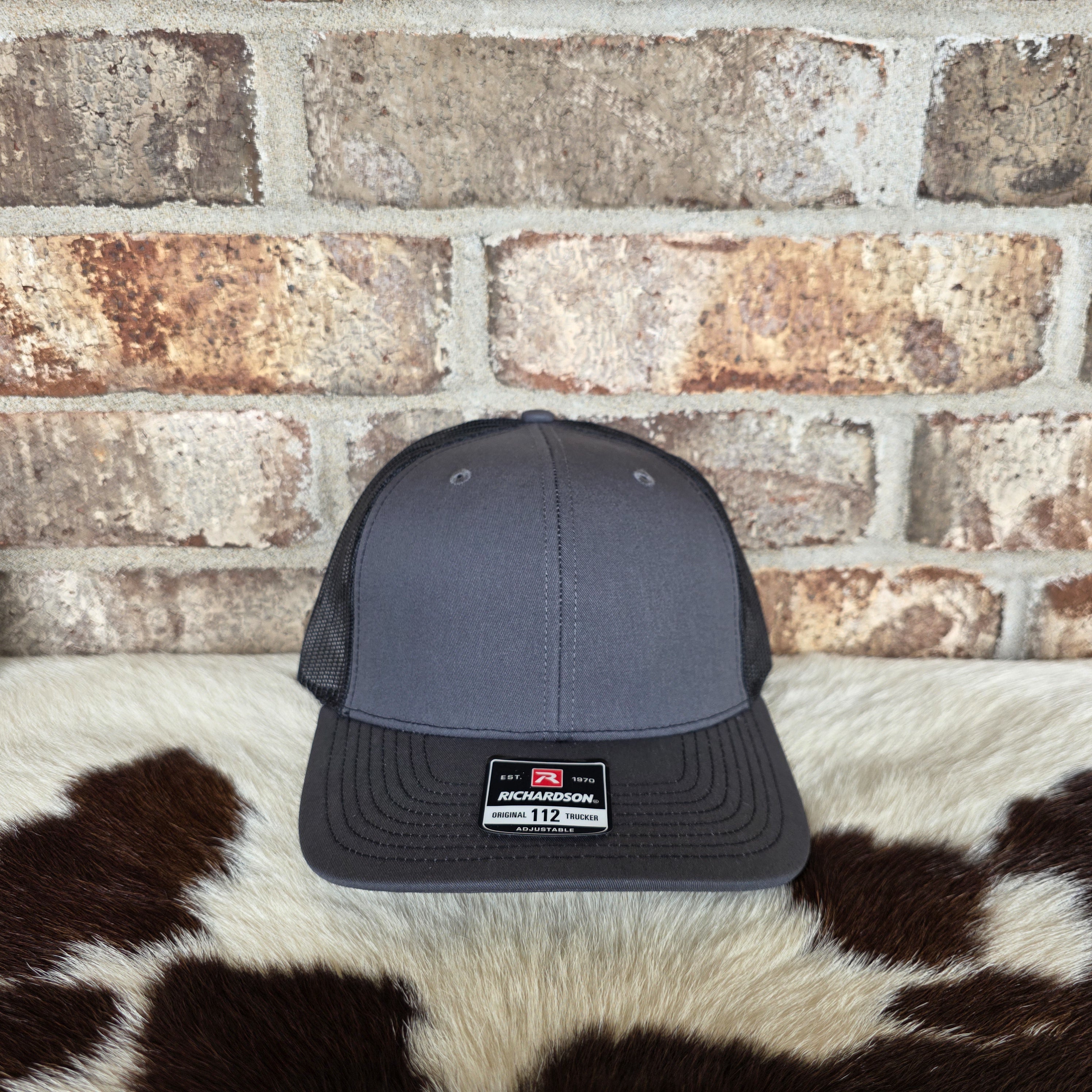 Gray trucker cap with a logo on a cowhide rug against a brick wall