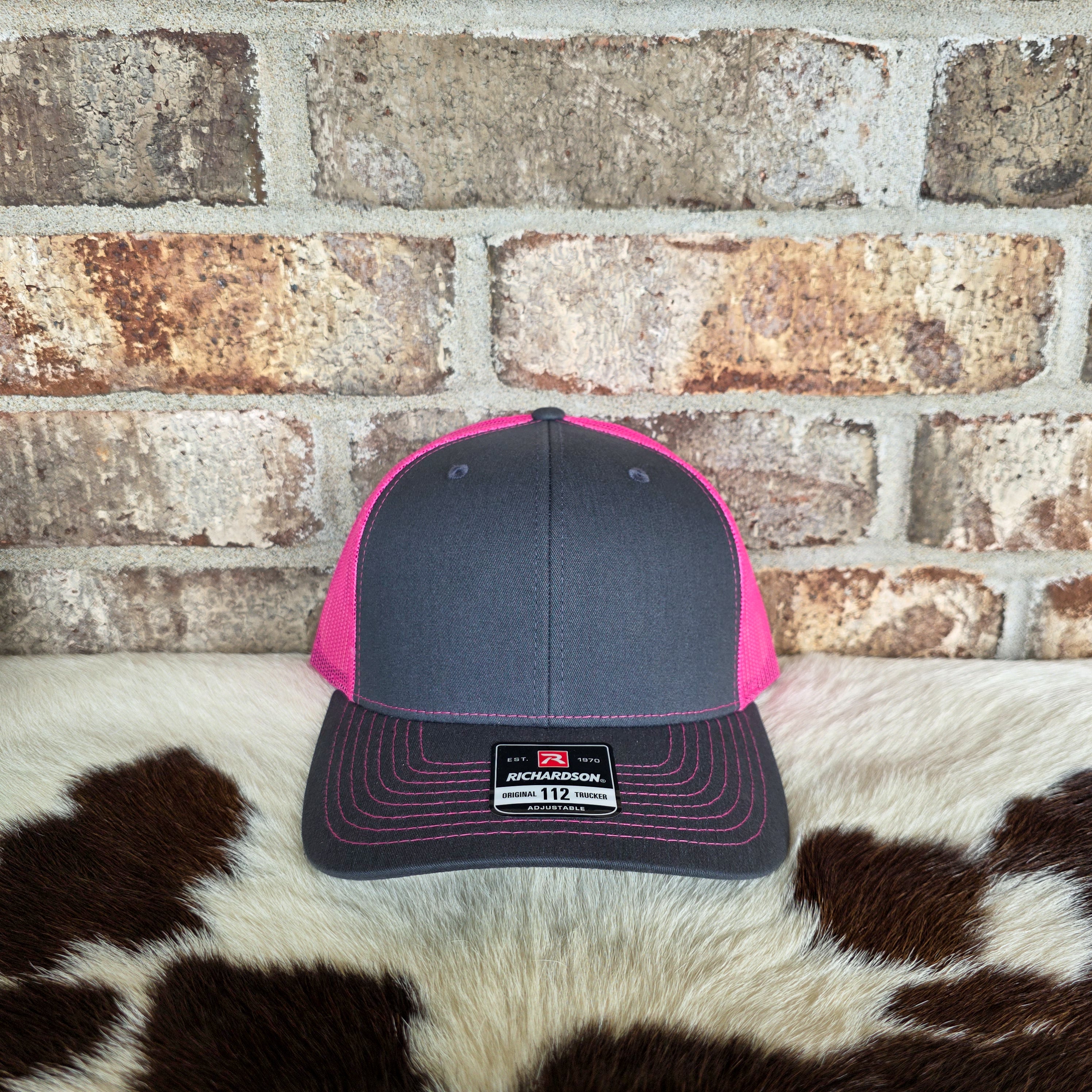 Gray and pink cap with Richardson logo on a cowhide rug against a brick wall.