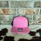 Pink and black cap on a cowhide rug with a brick wall background