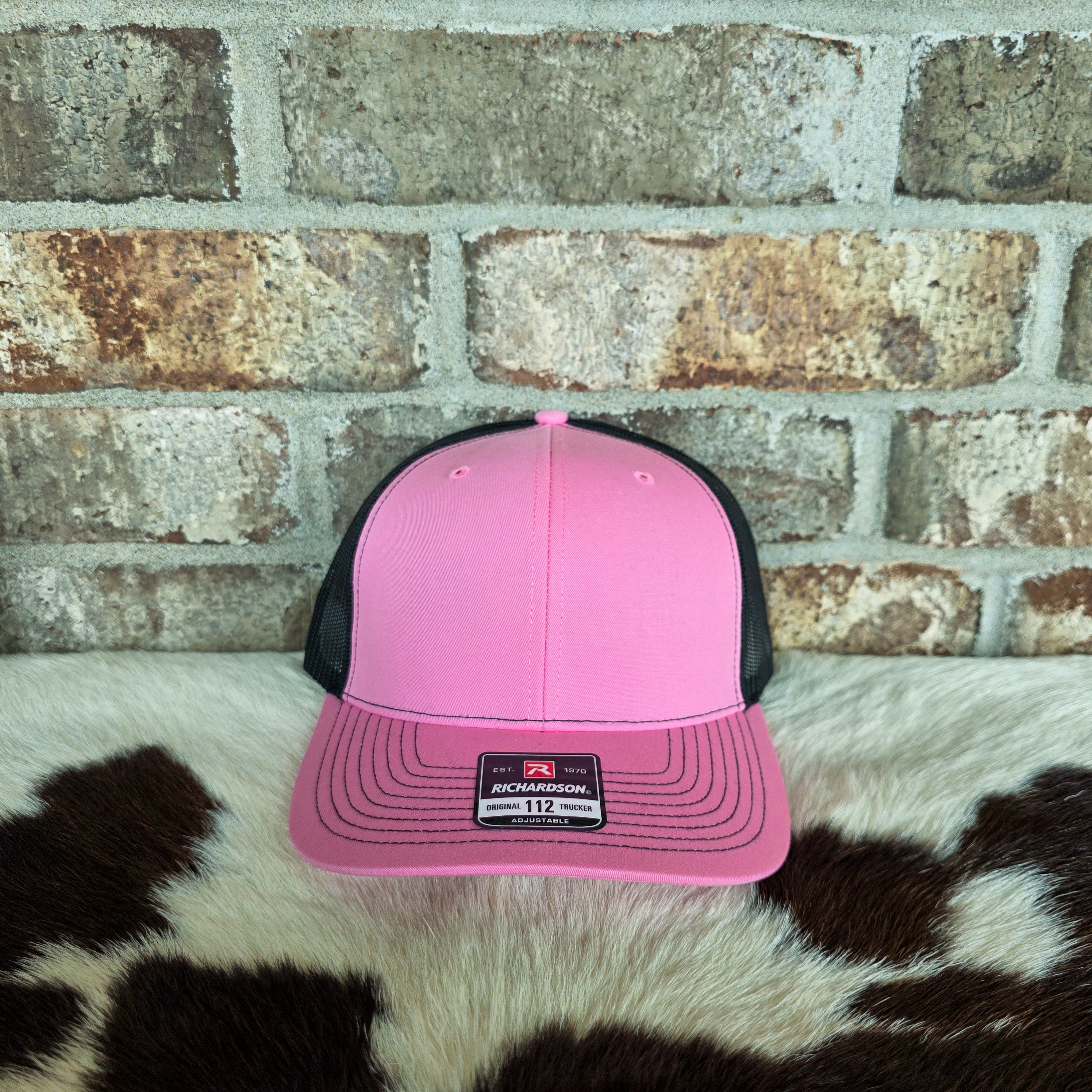 Pink and black cap on a cowhide rug with a brick wall background