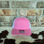 Pink and white cap with a logo on a cowhide rug against a brick wall