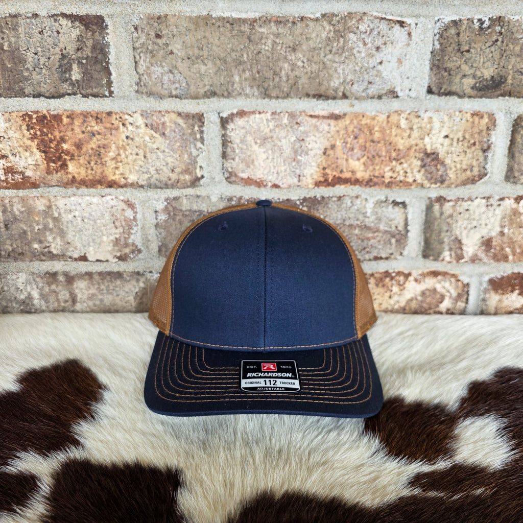 Navy and brown cap on a cowhide rug with a brick wall background