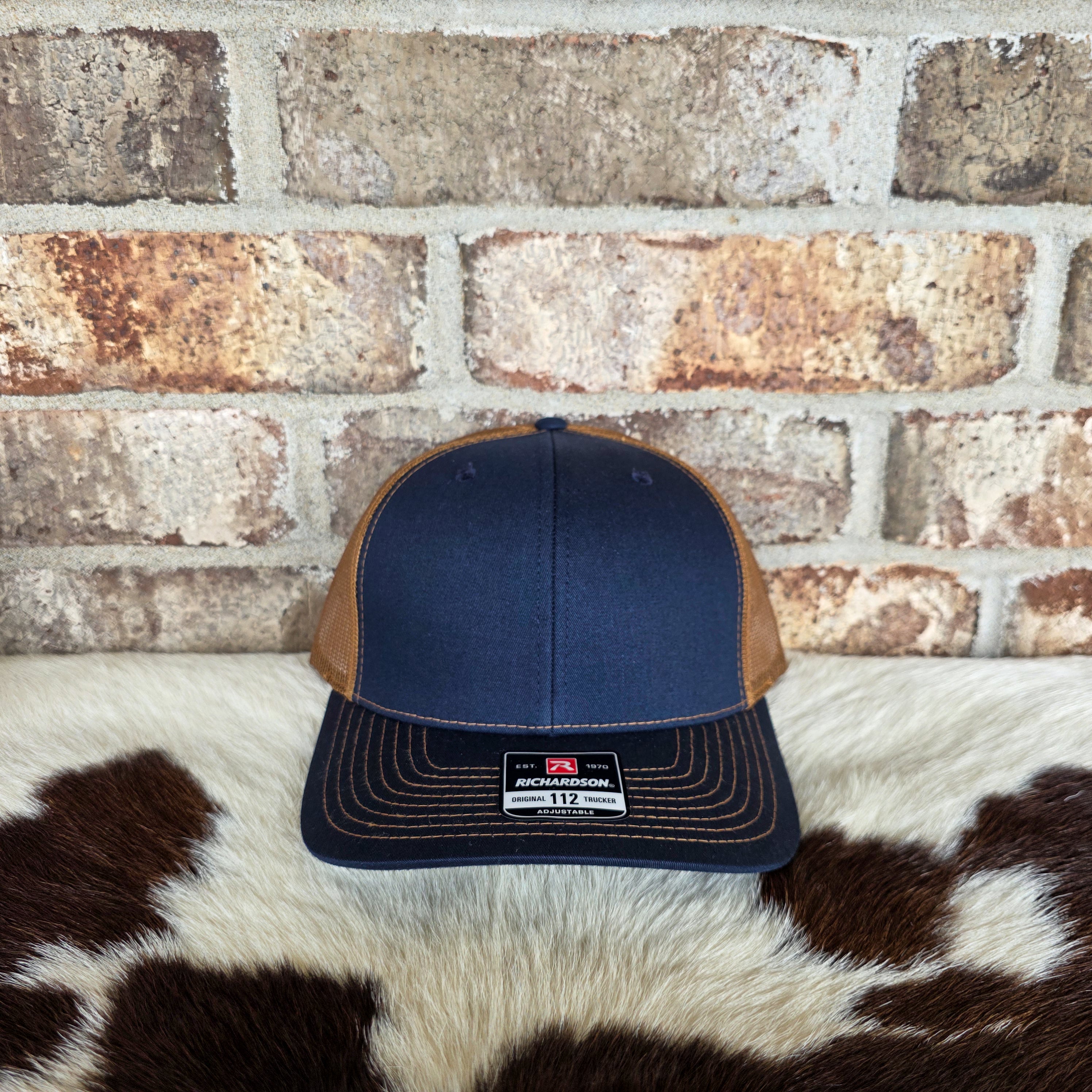 Navy and brown cap on a cowhide rug with a brick wall background